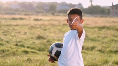 Elinde top olan Afrikalı bir çocuk yaz tarlasında baş parmağını gösteriyor.