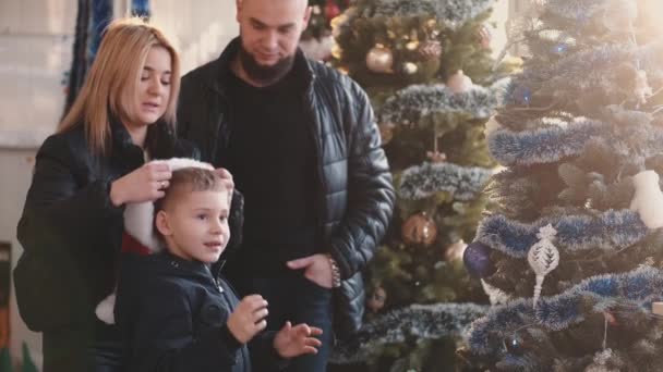 Mamá poniendo sombrero de santa en la cabeza hijos en la tienda — Vídeo de stock