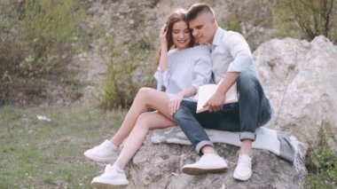 Erkek ve kadın taşın üzerinde oturup birlikte kitap okuyorlar.