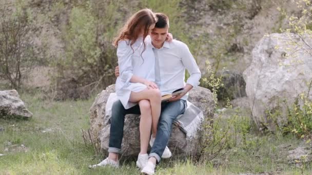 Hombre y mujer sentados en piedra y leyendo un libro juntos — Vídeos de Stock