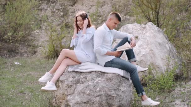 Hombre y mujer sentados en piedra y leyendo un libro juntos — Vídeo de stock