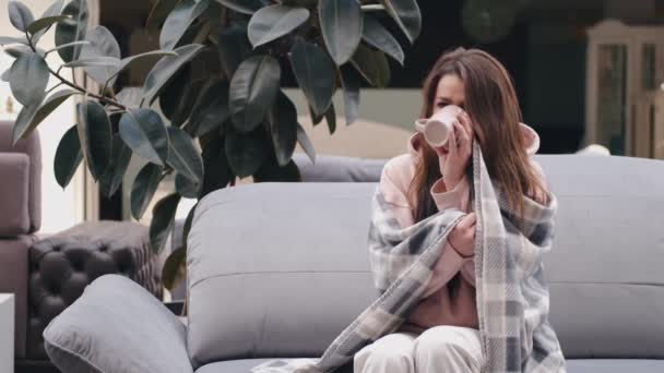 A mulher doente está sentada no sofá embrulhada em cobertor e bebendo remédio — Vídeo de Stock