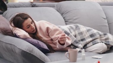 Kendini hasta hisseden kadın yatakta yatıyor ve sıcaklığı kontrol ediyor.