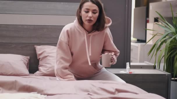 Красива молода жінка залишиться в ліжку і вип'є трохи чаю — стокове відео