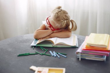 Kitaplarla dolu bir masada oturan küçük kız.