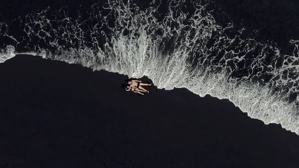 Pár leží na černém písku u oceánu — Stock fotografie