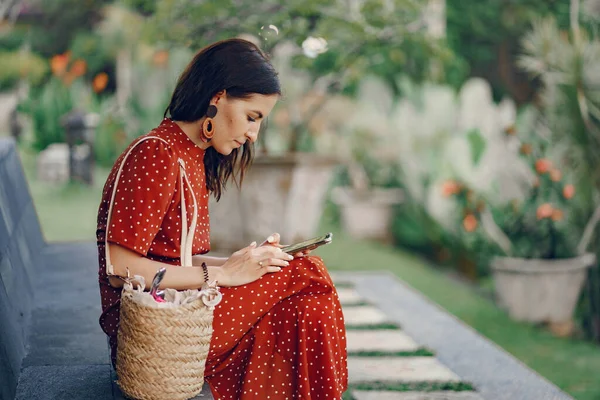 Девушка в красном платье сидит и пользуется телефоном — стоковое фото