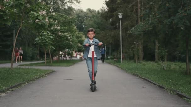 Schooljongen paardrijden een scoother op de weg in een park — Stockvideo