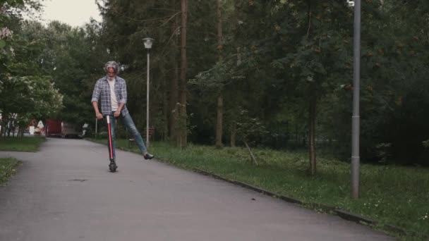 Stilvoller Senior, der in einem Park mit einem Roller unterwegs ist — Stockvideo