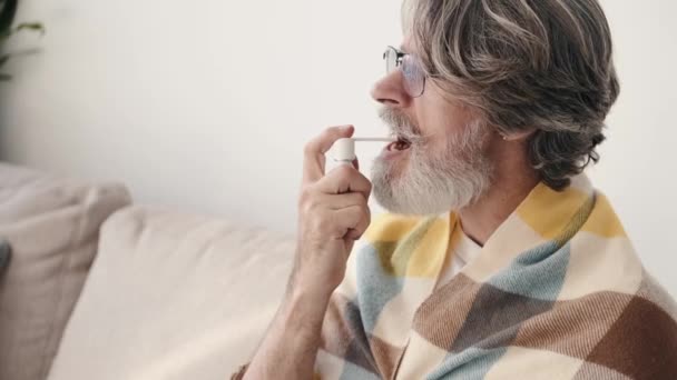 Öreg ember becsomagolva egy takaró permetező gyógyszert a torokba — Stock videók