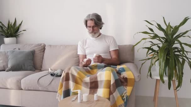 Симпатичный мужчина принимает таблетки, сидя на диване. — стоковое видео