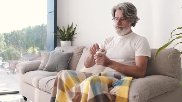 Good looking senior man taking in pills sitting on a couch — Stock Video