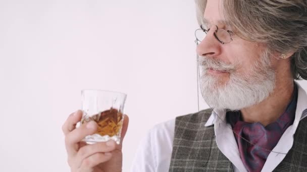 Homme âgé en lunettes regardant un verre de whisky — Video