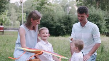 Ebeveynler ve iki oğlu parkta çimlerin üzerinde oturuyorlar.