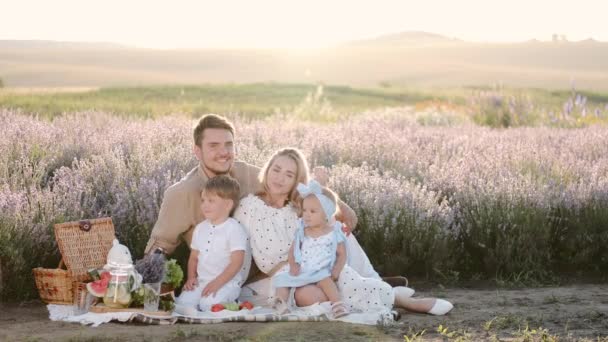 Liebevolle Familie mit Kindern sitzt bei Sonnenuntergang auf einer Decke im Lavendelfeld — Stockvideo
