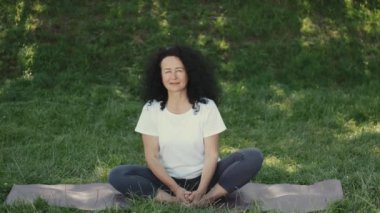 Orta yaşlı bir kadın parkta sabah yoga yapıyor.