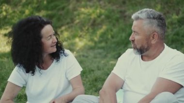 Kıdemli çift, çimlerin üzerinde oturmuş birbirlerine bakıyorlar.