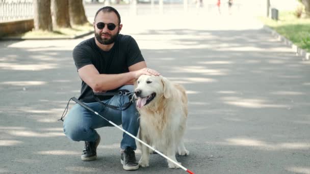 Uomo barbuto cieco con bastone e labrador seduto sul marciapiede nel parco — Video Stock