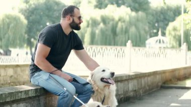 Kılavuz köpekli, parktaki bankta oturan kör, olgun bir adam.