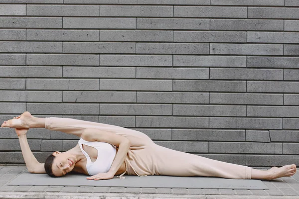 Femme pratiquant le yoga avancé contre un mur urbain sombre — Photo