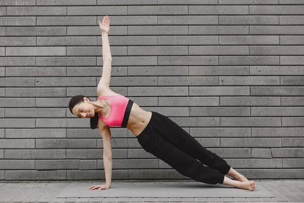 Femme pratiquant le yoga avancé contre un mur urbain sombre — Photo