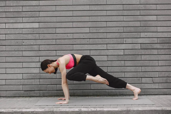 Mulher praticando ioga avançado contra uma parede urbana escura — Fotografia de Stock