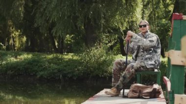 Özel üniformalı ve güneş gözlüklü bir genç göl kıyısında balık tutuyor.