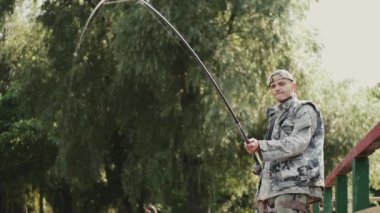 Özel üniformalı bir adam parktaki ahşap iskelede balık tutuyor.