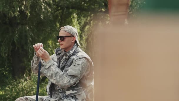Mladý muž ve speciální uniformě a sluneční brýle rybaření na molu u jezera — Stock video