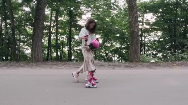 Madre e hija en patines y casco están en la carretera en un parque — Vídeo de stock