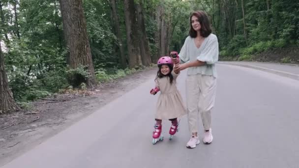 Madre e hija en patines y casco están en la carretera en un parque — Vídeo de stock