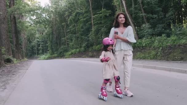 Mother and daughter in rollerblades and helmet are on the road in a park — Stock Video