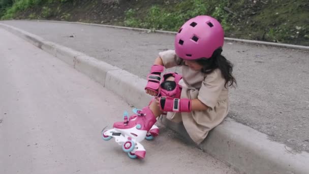 Mała dziewczynka w kasku stawia sprzęt ochronny na drodze — Wideo stockowe