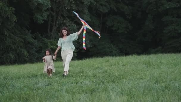 Feliz madre e hija caminando con cometa en el césped — Vídeo de stock