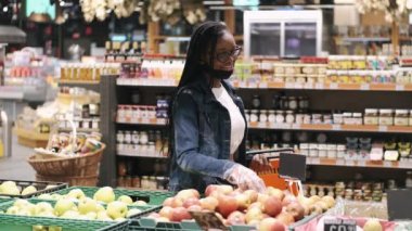 Maskeli Afro-Amerikalı genç kadın süpermarketten yiyecek seçiyor.