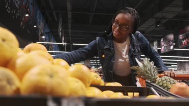 Siyah genç bir kadın süpermarkette portakal seçiyor.