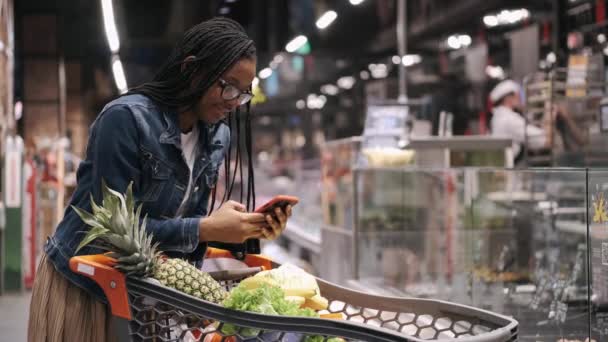 Africana america chica con teléfono y carro en un supermercado — Vídeo de stock