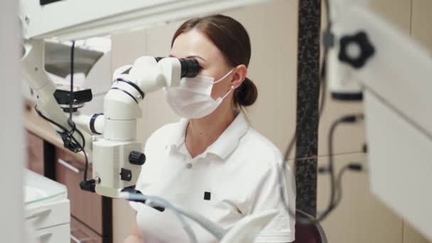 Uma endodontista feminina está tratando canais ao microscópio. — Vídeo de Stock