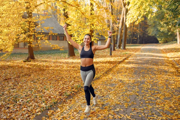 Chica deportiva en un entrenamiento negro en un parque de otoño — Foto de Stock