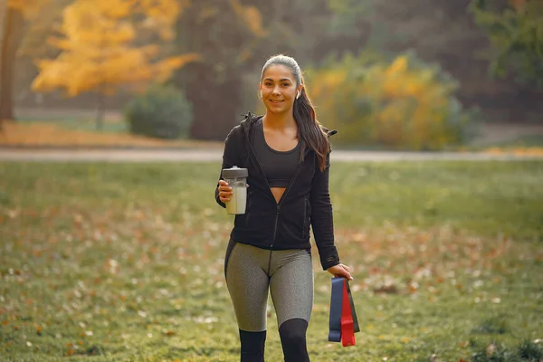 Спортивная девушка в черном топе тренируется в осеннем парке — стоковое фото