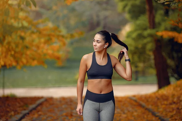 Chica deportiva en un entrenamiento negro en un parque de otoño — Foto de Stock