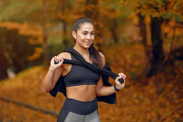 Chica deportiva en un entrenamiento negro en un parque de otoño — Foto de Stock