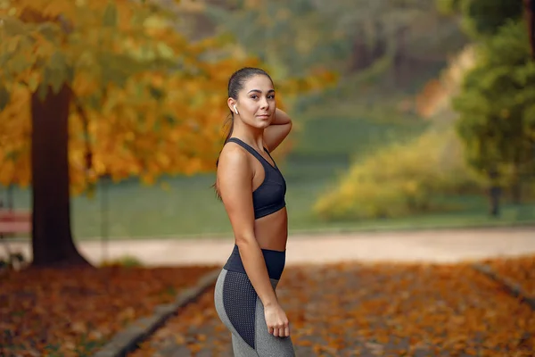 Chica deportiva en un entrenamiento negro en un parque de otoño — Foto de Stock