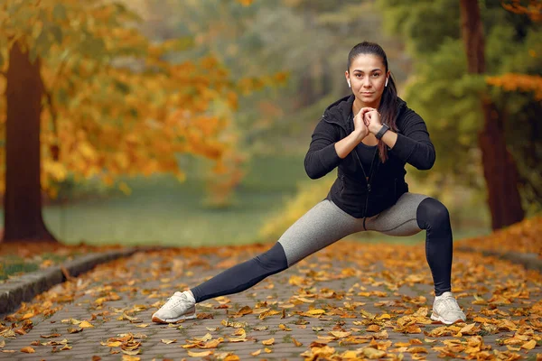 Chica deportiva en un entrenamiento negro en un parque de otoño — Foto de Stock