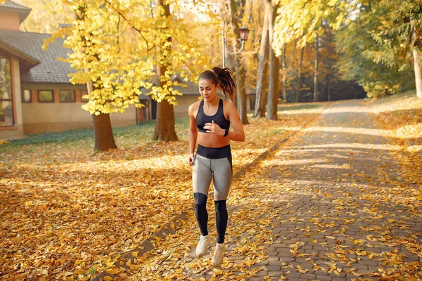 Chica deportiva en un entrenamiento negro en un parque de otoño — Foto de Stock