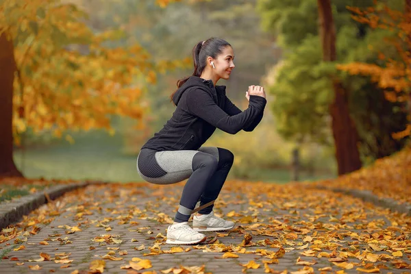 Menina de esportes em um treinamento de topo preto em um parque de outono — Fotografia de Stock