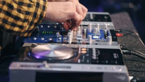 Primer plano de manos de DJ controlando una mesa de música en un club nocturno — Vídeo de stock