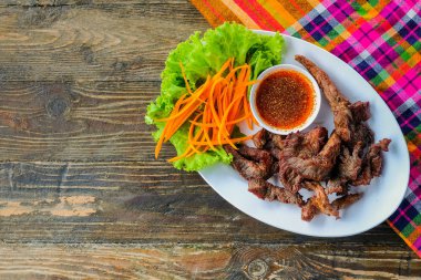 Sebze ve ahşap bir masa üzerinde daldırma sos ile beyaz bir tabak içinde sığır eti.