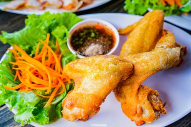 Sebze ve ahşap bir masa üzerinde daldırma sos ile beyaz bir tabak kızarmış tavuk.