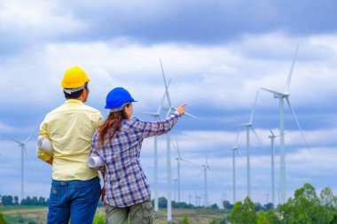 Mühendis ve yöneticilerle toplanan erkek ve kadın inşaat alanının planlarını okuyorlar..